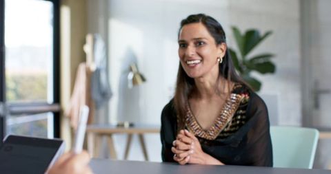 Indian businesswoman smiling and leaning forward during collaborative meeting at office