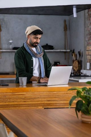 Asian man working on laptop at modern rustic kitchen island with mug