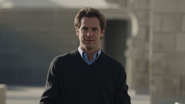 Confident businessman standing in urban courtyard in light blue shirt and dark sweater