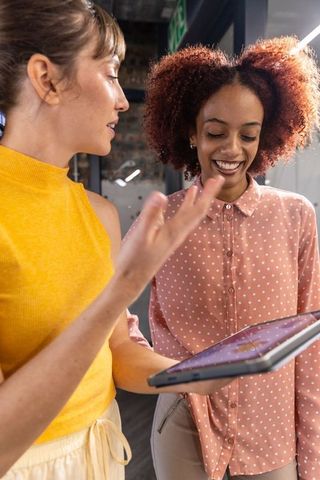Diverse coworkers analyzing tablet in modern office hallway