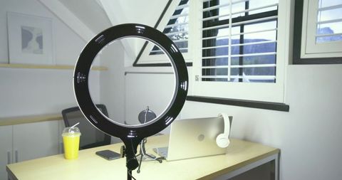 Led ring light illuminating minimalist home workspace with laptop, headphones, shutters