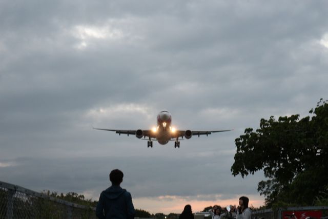 Airplane descending against a cloudy sky during early dawn with a runway lined by spotters observing the landing. Ideal for travel-related content, aviation blogs, airport services, airline advertisements, and promotional material for travel and tourism.