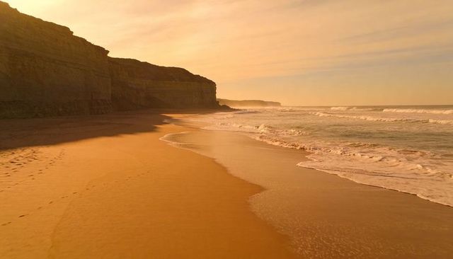 Golden-hour cliffs and deserted beach stretching into misty horizon