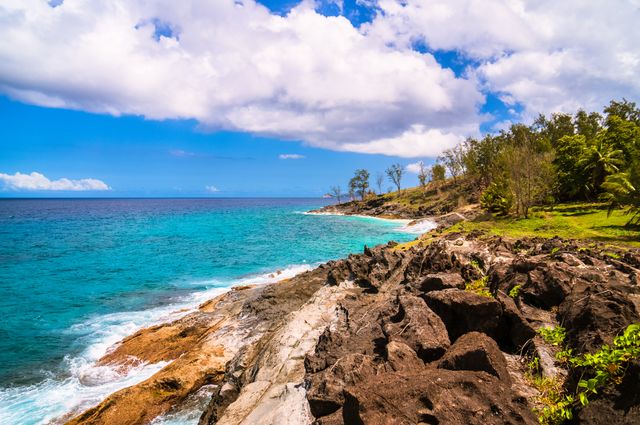 Ideal for travel brochures, websites, and advertisements promoting beach destinations, tropical vacations, or nature photography. This photo highlights the natural beauty of the seashore with its clear blue water and rocky coastline.