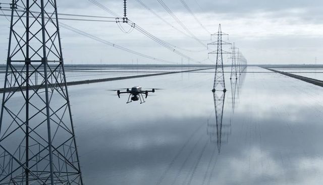 Inspection drone hovering over flooded power line corridor with reflective pylons