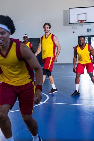 Diverse athletes practicing defensive skills on indoor basketball court