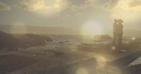 Romantic Couple Embracing on Rocky Shoreline at Serene Sunset