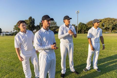 Young cricket players standing on sunlit outfield wearing white uniforms and caps