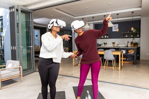 Holding hands while experiencing virtual reality with white vr headsets in modern open-plan home
