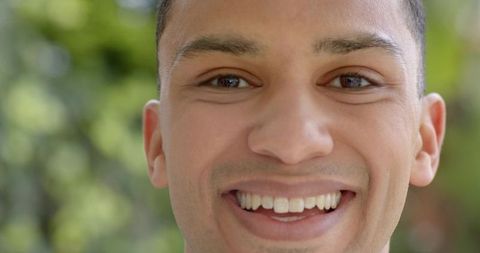Close-up smiling young man enjoying sunny park with soft bokeh green background