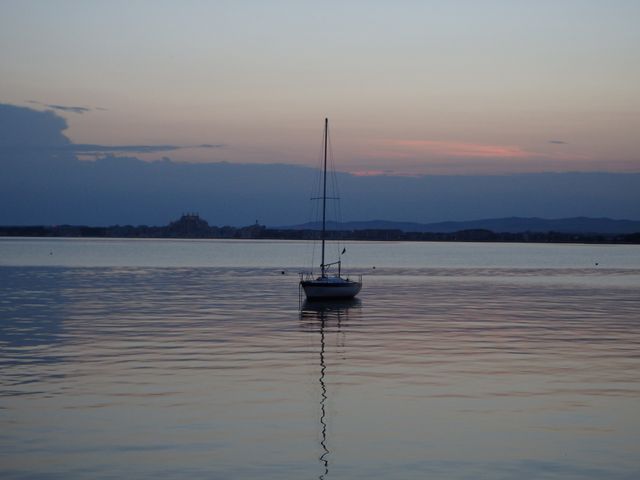 Sailboat anchored in still waters during twilight, with a serene sunset in the background and tranquil reflection on the water. Ideal for travel magazines, relaxation themes, nature posters, and backgrounds promoting peacefulness and tranquility.