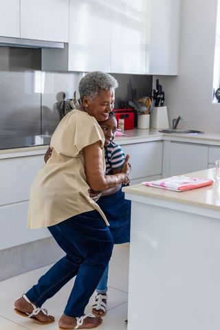 Senior african american grandmother hugging granddaughter in sunlit modern kitchen