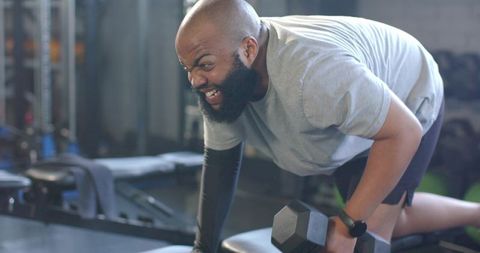 African american man performing intense one-arm dumbbell row on bench for workout