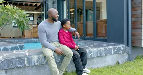 African american father and son sharing moment on modern patio beside reflecting pool, family bond