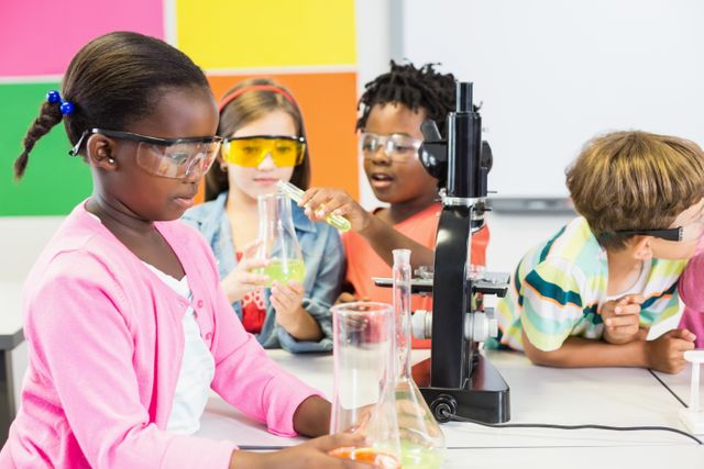 Children engaged in a science experiment in a classroom setting, wearing safety goggles and using laboratory equipment such as beakers and a microscope. Ideal for educational content, school brochures, STEM program promotions, and articles on childhood education and teamwork.