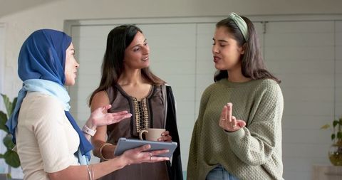 Diverse female colleagues collaborating over tablet in modern office lounge casual meeting
