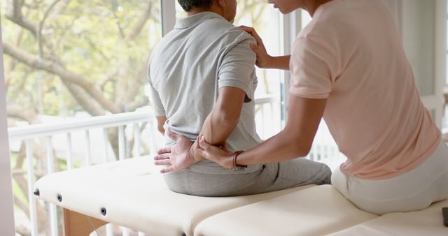 Physiotherapist assessing mature patient's back pain in bright clinic. Suitable for use in medical articles, health care professions marketing, and wellness programs content.
