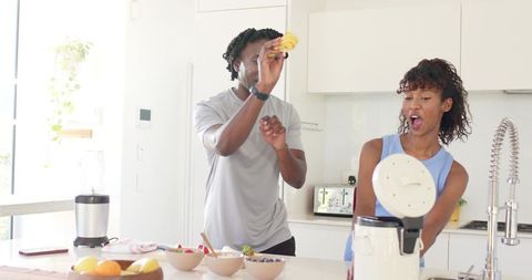 African american couple preparing fresh fruit smoothie together in bright modern kitchen