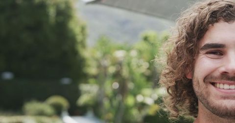 Young Man with Curly Hair Smiling Outdoors in Garden