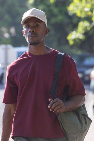Urban commuter walking with backpack wearing maroon tee and beige cap on sunlit street