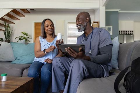 African-american home nurse consulting patient on medication using tablet in living room