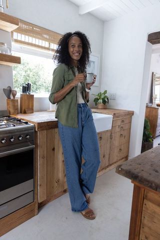 African american woman sipping coffee leaning on rustic countertop in farmhouse kitchen