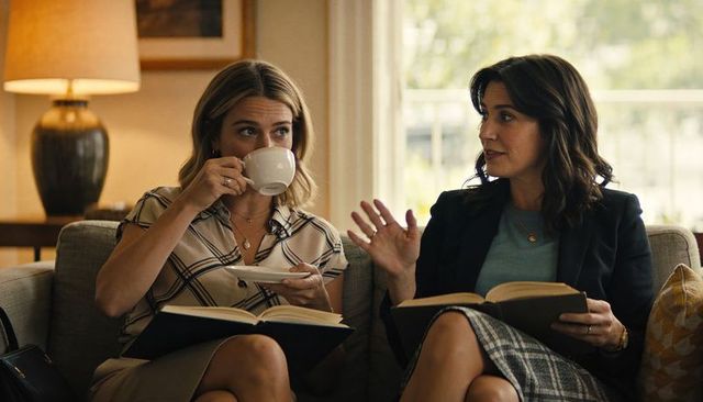 Two women sharing coffee and book discussion on cozy living room sofa, casual conversation