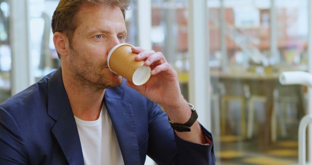 Man drinks coffee in a stylish, modern office. He appears focused and relaxed, likely taking a break from work. Ideal for business, corporate lifestyle, and workplace wellness use.