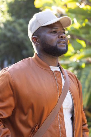 African american man enjoying sunny park stroll in beige cap and brown bomber jacket