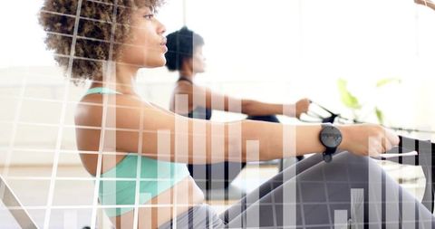 Indoor rowing workout with smartwatch, women training on ergometer in bright fitness studio
