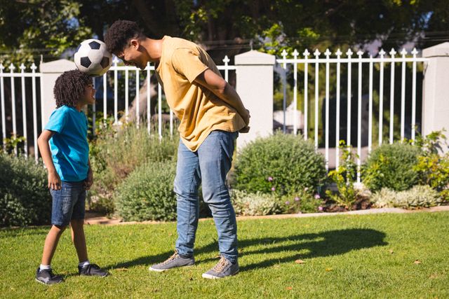 Full length of hispanic father and son heading soccer ball while playing at backyard on sunny day. unaltered, sport, enjoyment, family, lifestyle and togetherness concept.