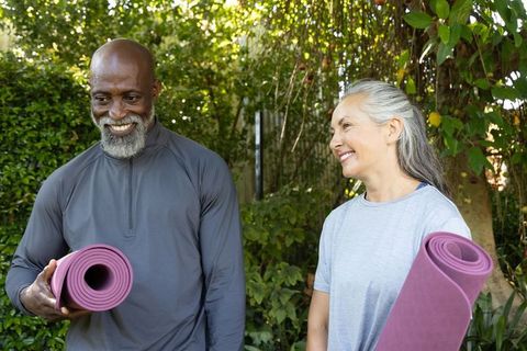 Mature adults holding purple yoga mats and smiling while preparing for outdoor yoga class