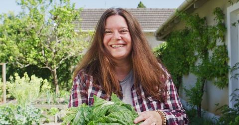 Smiling Caucasian Woman Holding Fresh Lettuce in Garden