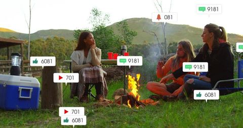 Friends gathering around campfire at dusk with floating social media icons