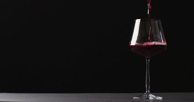 A stream of red wine pouring into a crystal glass against a black background, creating a sense of luxury and elegance. Ideal for use in advertisements or websites related to wine, fine dining, celebrations, or gourmet products. Also suitable for illustrating concepts of relaxation, social events, and winemaking.