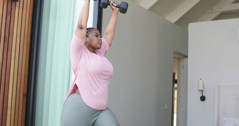 African american woman lifting dumbbells in bedroom for home strength workout and motivation