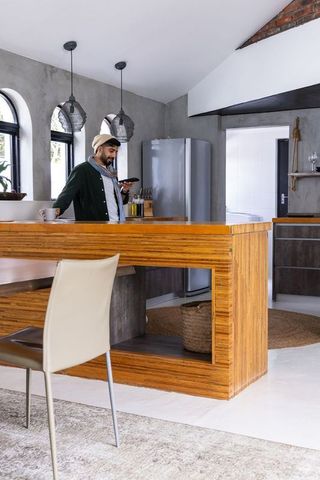 Man using smartphone in sunlit contemporary loft kitchen with wooden island and brick accents