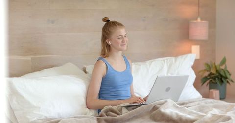 Woman in Relaxed Home Setting Smiling While Using Laptop in Bed