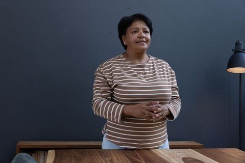 Senior woman in striped sweater standing by wooden desk in minimalist office