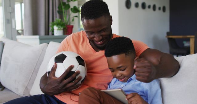 African american father and son cheering together while watching sports on digital tablet at home. family father son togetherness relationship concept