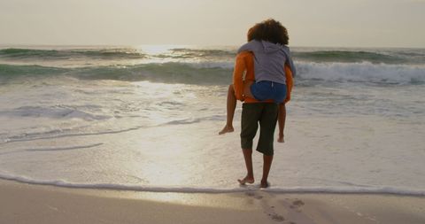 Couple Enjoying Piggyback Ride by Ocean at Sunrise