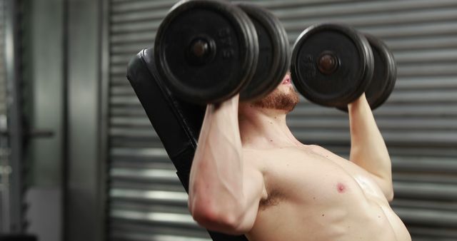 A dedicated young man intensifies his upper body strength by lifting dumbbells on a bench. - Download Free Stock Photos Pikwizard.com