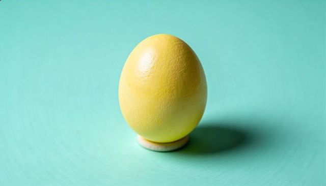 Yellow painted egg standing on white egg cup on teal background minimal still life studio