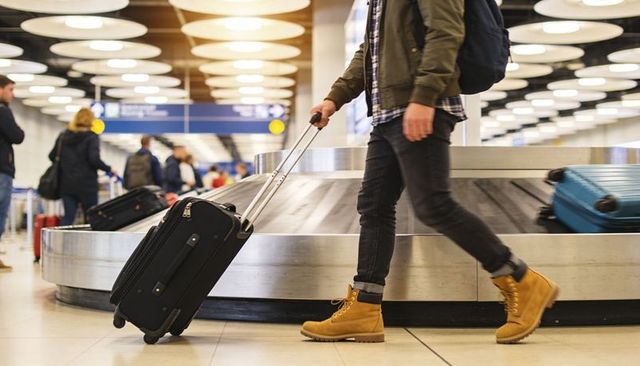 Traveler walking with rolling suitcase past airport baggage carousel