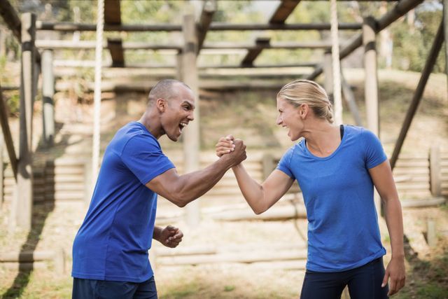Fit man and woman greeting each other with enthusiasm during an outdoor obstacle course in a boot camp. Both are wearing athletic clothing and appear motivated and energetic. This image can be used for promoting fitness programs, teamwork activities, outdoor training sessions, and motivational fitness content.
