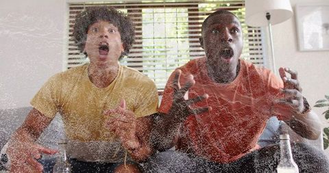 Two friends reacting to game on couch, surprised faces, living room watch party reaction