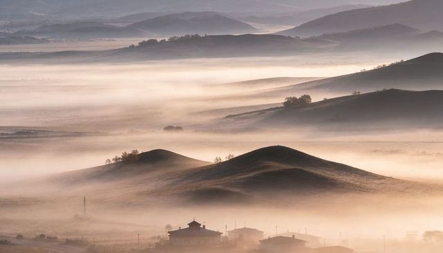 Fog-filled rolling hills at sunrise revealing misty rural valley rooftops and ridges