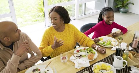 Family Sharing Healthy Meal at Sunlit Dining Table, Mother Talking While Daughter Smiling