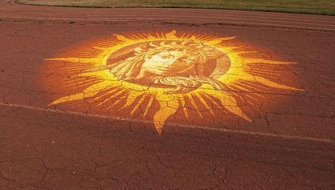 Golden sun mural featuring stylized female face painted on weathered red running track