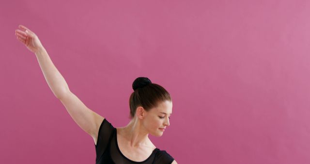 A young Caucasian female dancer is practicing ballet against a vibrant pink background, with copy space. Her poise and concentration reflect the discipline and grace of classical dance training.